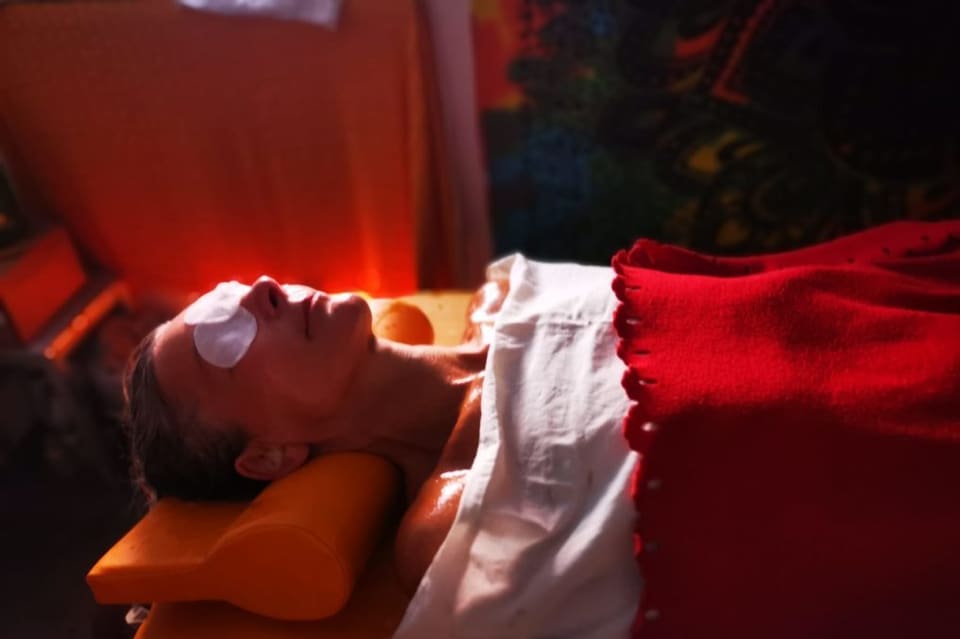 Eine Person ruht mit Augenauflagen unter einem roten Tuch bei warmem Licht