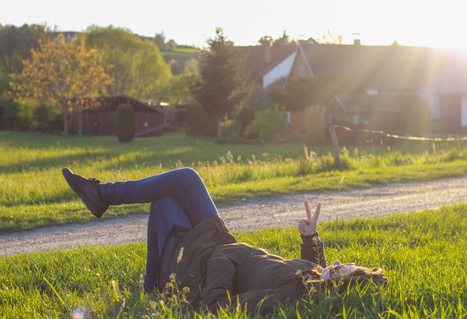 Bine Fetz liegt im Gras im Abendlicht und hebt eine Hand zum Peace-Zeichen