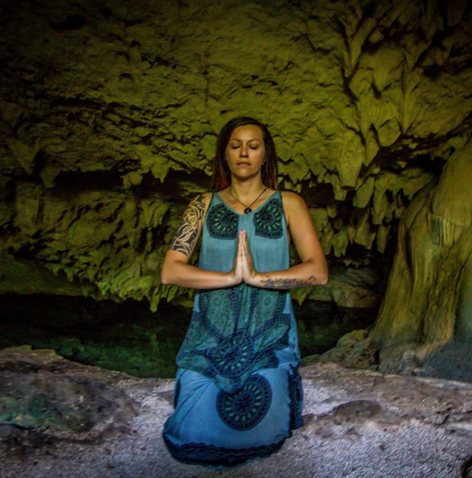 Bine Fetz sitzt mit gefalteten Händen in einer ruhigen Yogahaltung in einer Höhle